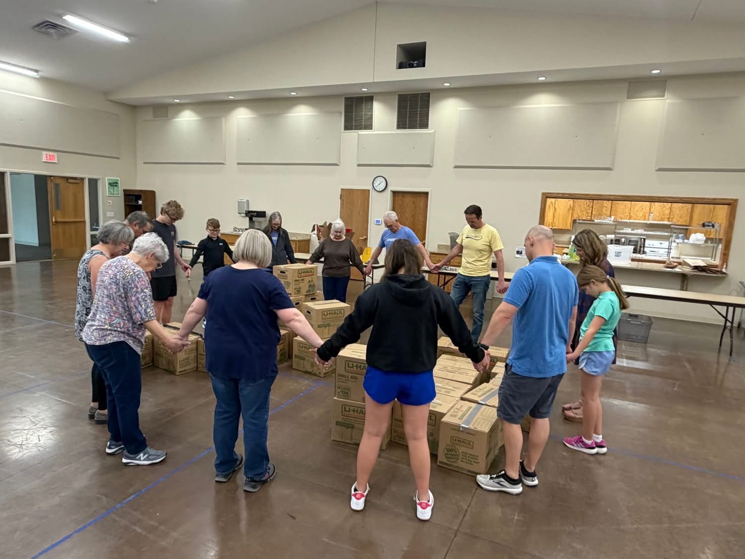 Volunteers of all ages joining hands in prayer before packing care packs in Wamego